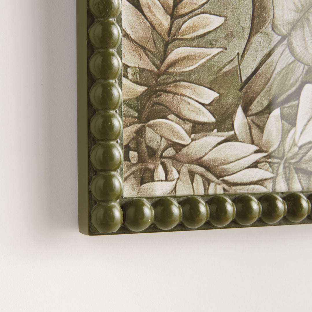 Close view of an olive green beaded frame corner around a parrot print, showing layered botanical artwork detail. Traditional