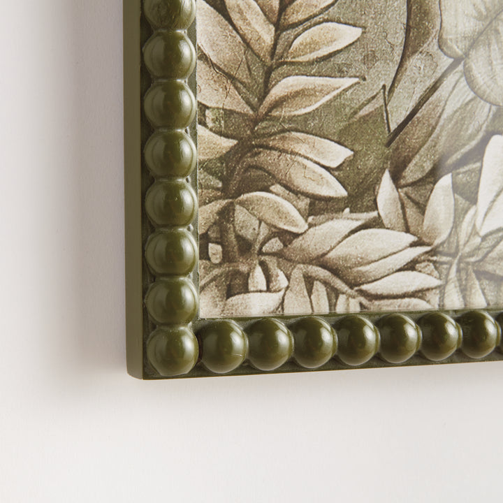 Close view of an olive green beaded frame corner around a parrot print, showing layered botanical artwork detail. Traditional