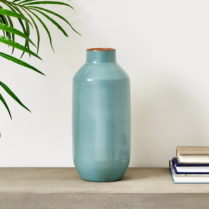 Pastel blue ceramic bottle vase with plant and books in background, artisan-made decor accent
