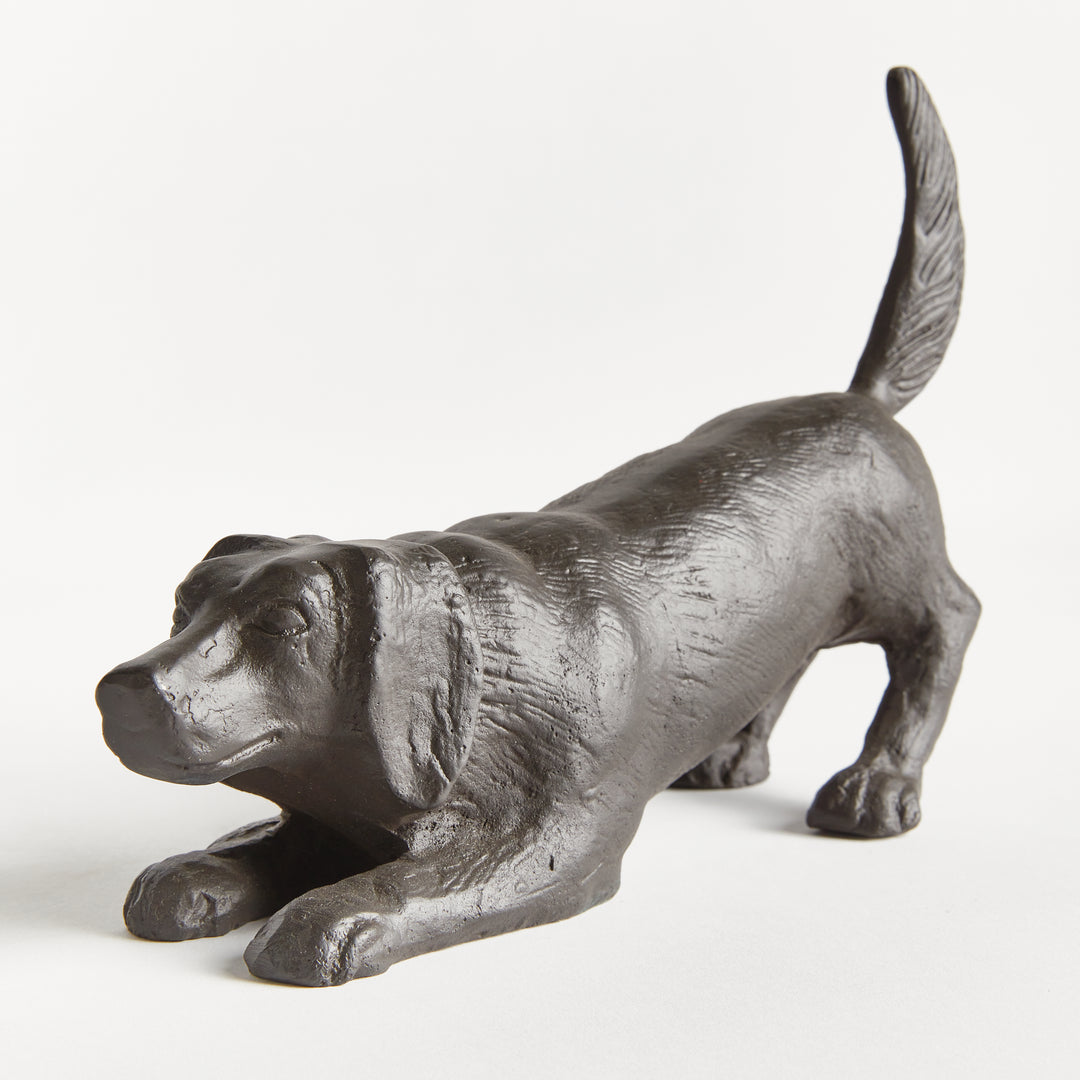 Three-quarter view of playful dog sculpture in black aluminum emphasizing movement, stance, and sculptural form.