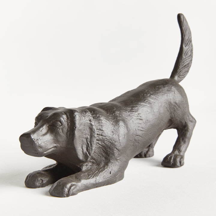 Three-quarter view of playful dog sculpture in black aluminum emphasizing movement, stance, and sculptural form.