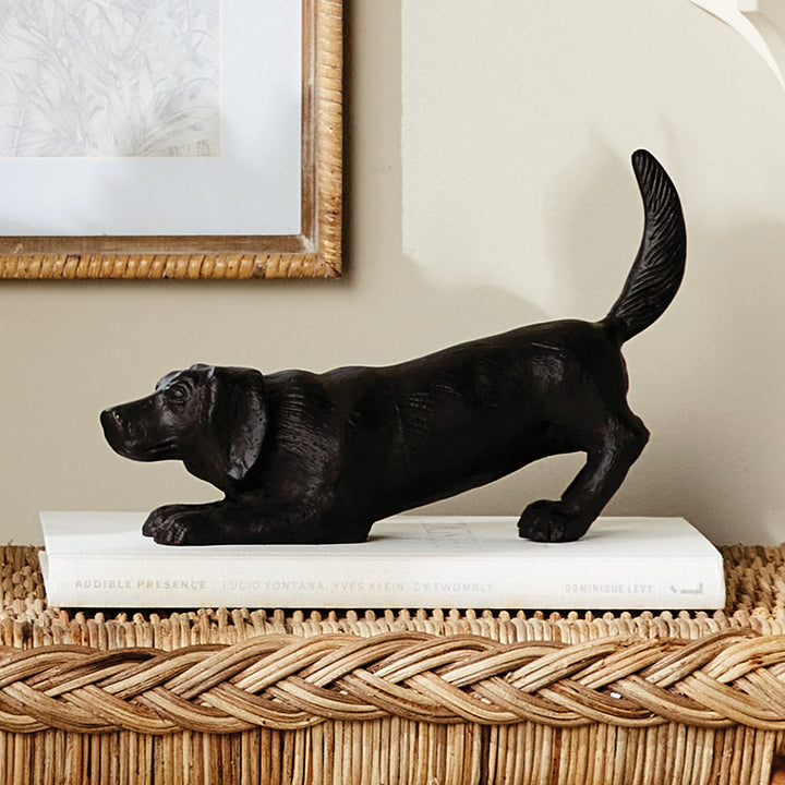 Playful dog sculpture in black aluminum displayed on a stack of books as a decorative accent for shelves or consoles.