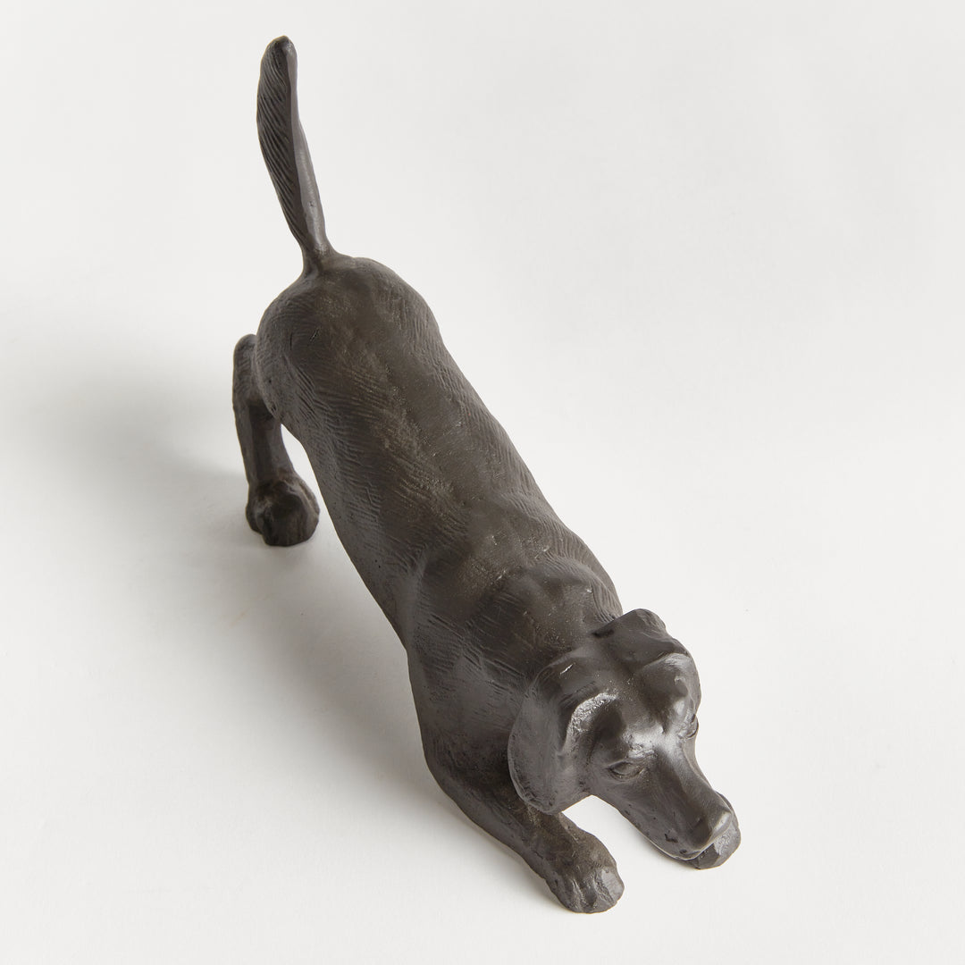 Rear angle of playful dog sculpture showing raised tail and textured black aluminum finish from above.