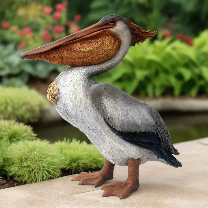 Large resin pelican sculpture in garden decor setting with colorful pond-side flowers