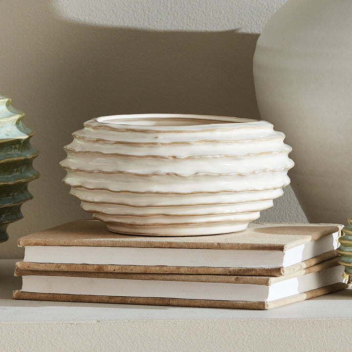 White ribbed ceramic decorative bowl on stacked neutral books, beside other pottery in a softly lit display - Modern Organic