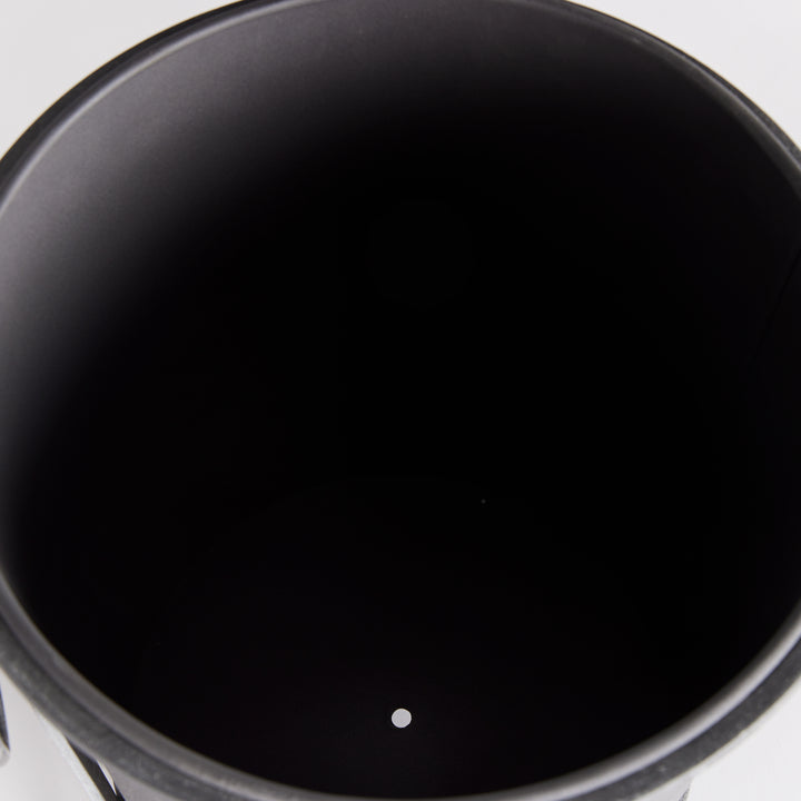 Small iron planter viewed from above, showing the dark inner liner and drainage opening at its base. Industrial Transitional