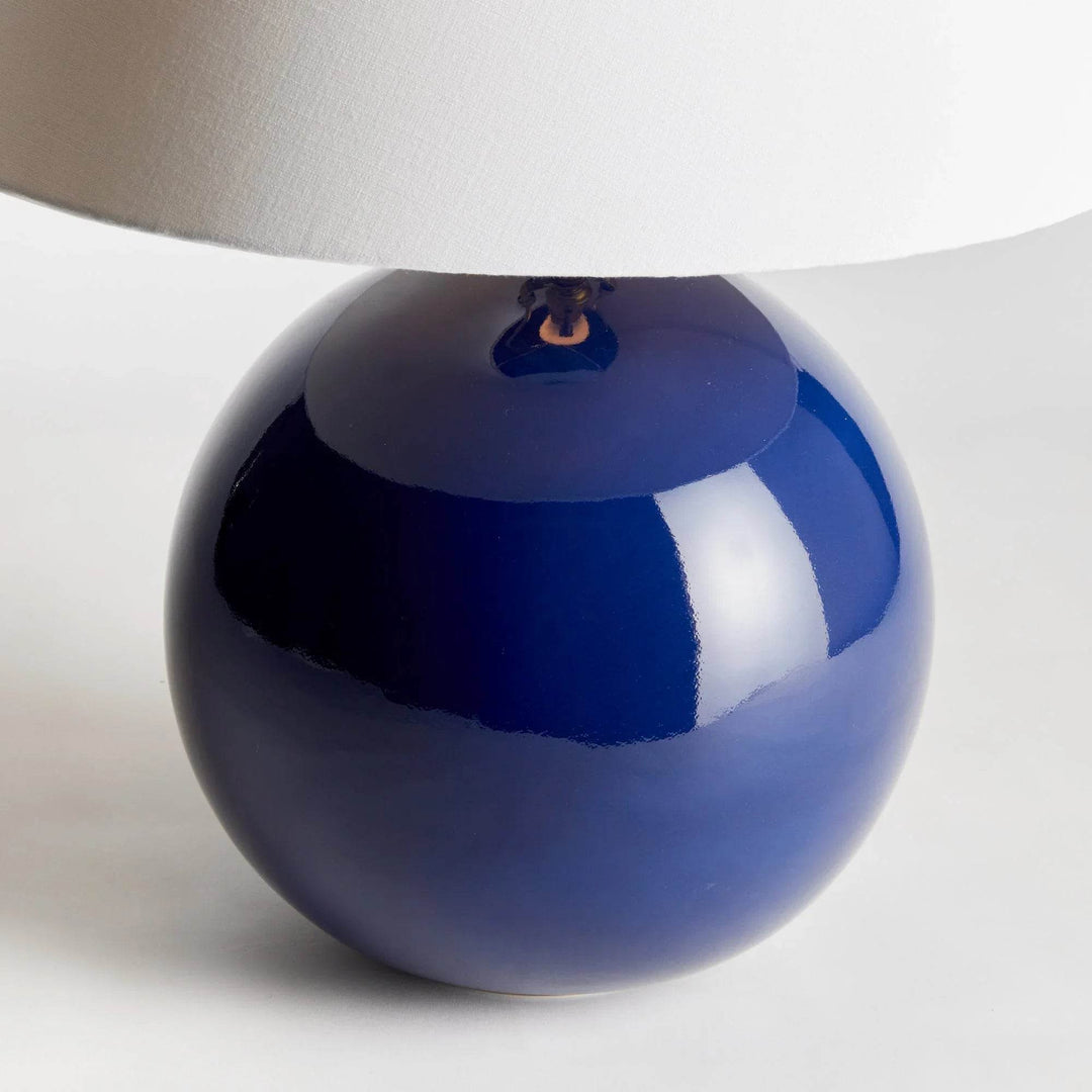 Detailed view of the rounded blue ceramic lamp base, showing reflective glaze beneath its white linen shade. Transitional