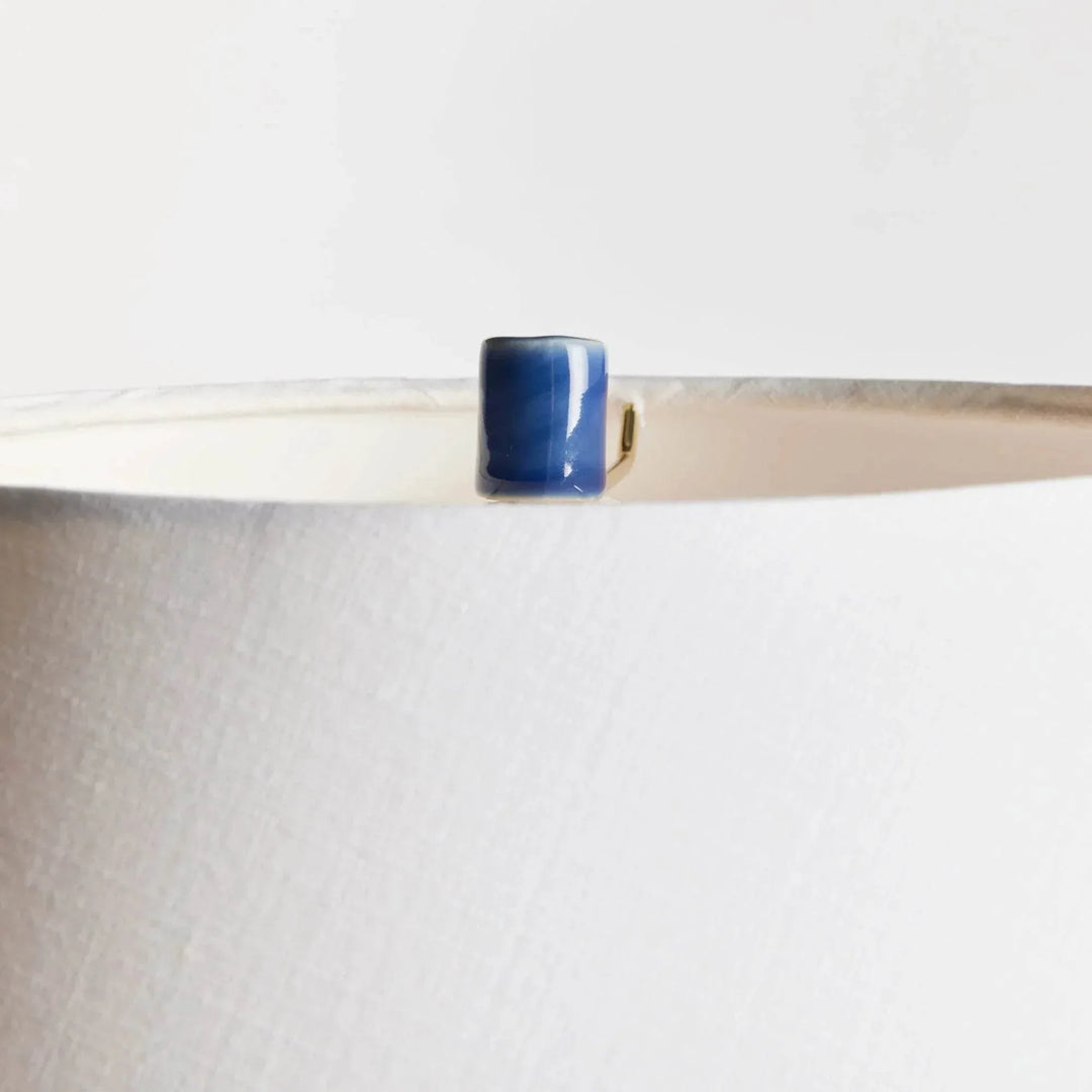 Detailed view of the blue ceramic finial above the white linen lamp shade, showing the fabric and upper rim. Transitional