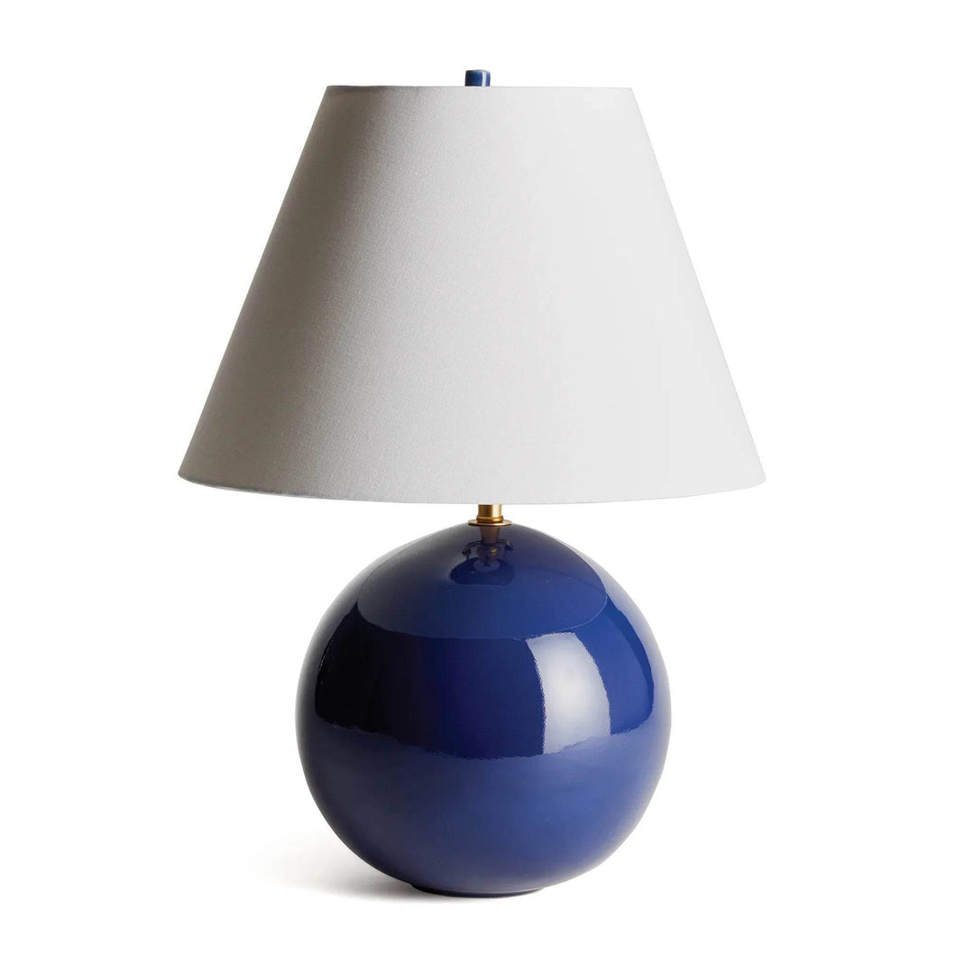 Round blue ceramic table lamp with a glossy spherical base and white linen empire shade on a pale background. Transitional