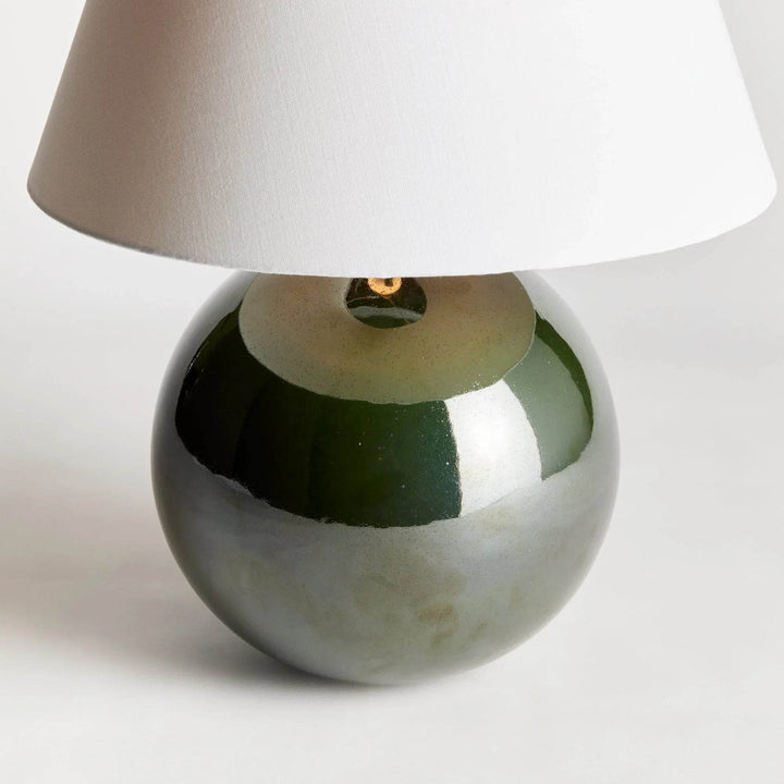 Detailed view of the rounded green ceramic lamp base, showing reflective glaze beneath its white linen shade. Transitional