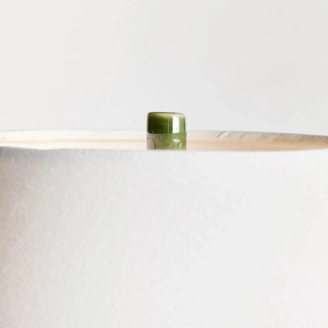 Detailed view of the green ceramic finial above the white linen lamp shade, showing the fabric and upper rim. Transitional
