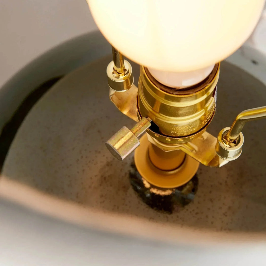 Detail of the rotary socket switch and illuminated bulb above the glossy green glazed ceramic table lamp base. Transitional
