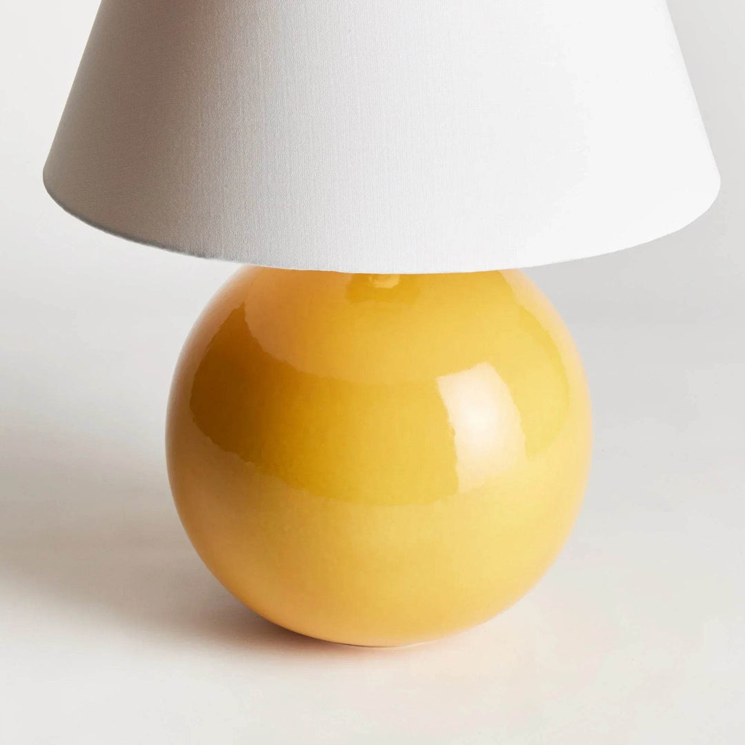 Close view of the rounded marigold ceramic lamp base, showing reflective glaze beneath its white linen shade. Transitional