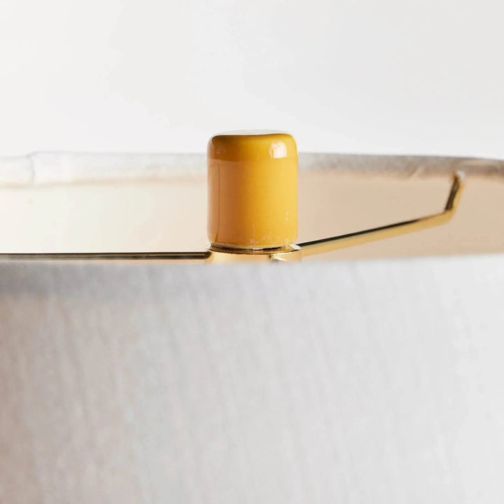 Close view of the marigold ceramic finial above the white linen lamp shade, showing the fabric and upper rim. Transitional