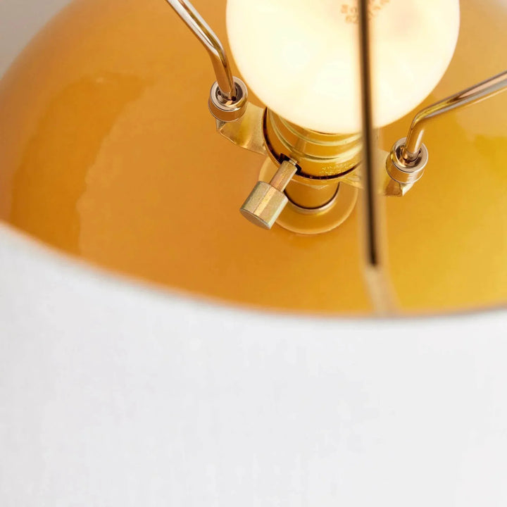 A close-up of the rotary socket switch and illuminated bulb above the glossy marigold ceramic table lamp base. Transitional