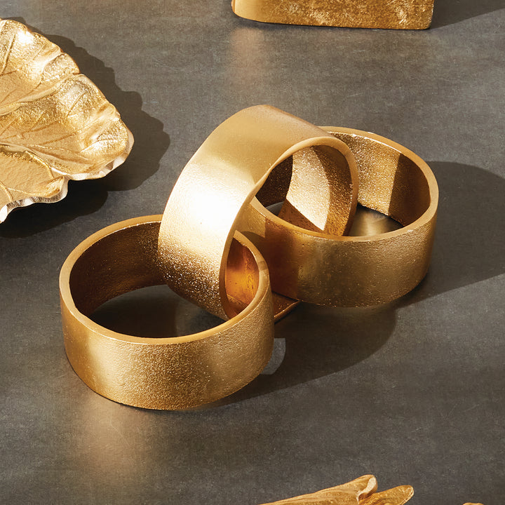 Gold chain-link sculpture on a dark tabletop, with three circular aluminum links beside gold accessories - Modern Organic