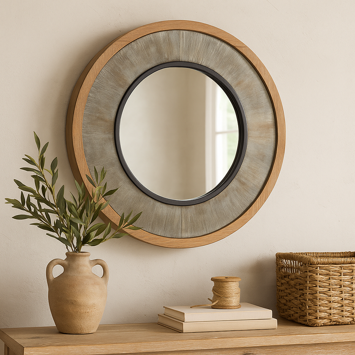 Round farmhouse mirror above a rustic console with olive branches, books, twine, and a woven basket in natural tones.

