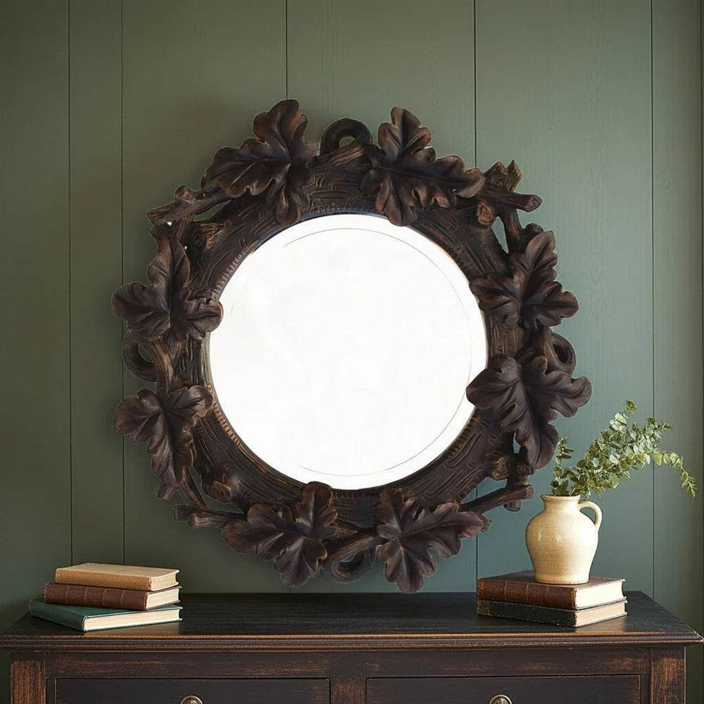 Beveled round wall mirror with oak leaf frame in rustic lodge style, styled above console against dark green vertical paneling.