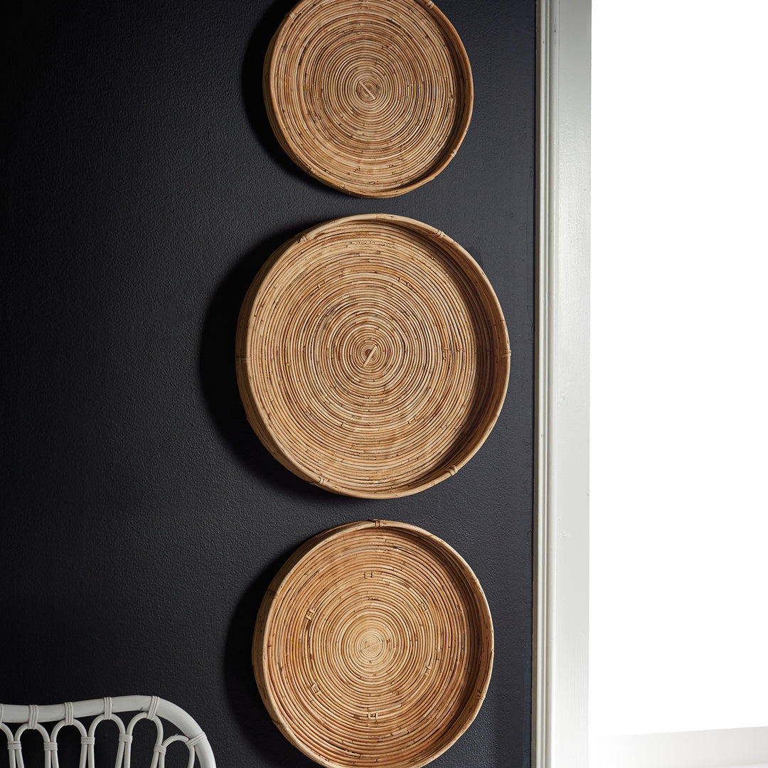 Close-up of circular woven cane tray hung on dark wall - boho natural basket wall accent