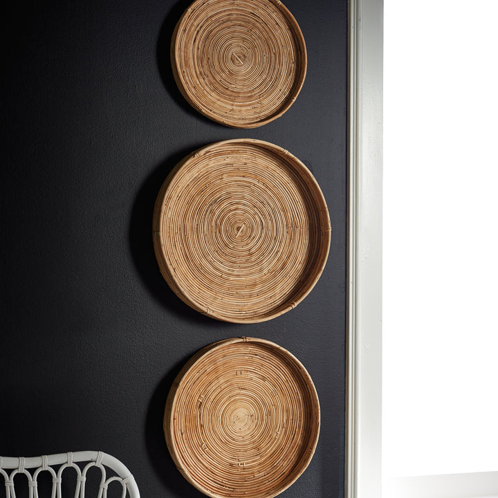 Close-up of circular woven cane tray hung on dark wall - boho natural basket wall accent