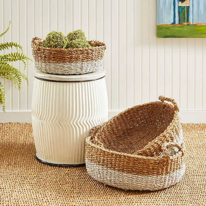 Seagrass basket set styled in living space with one basket stacked on a ceramic stool and another nested inside – Coastal Casual.

