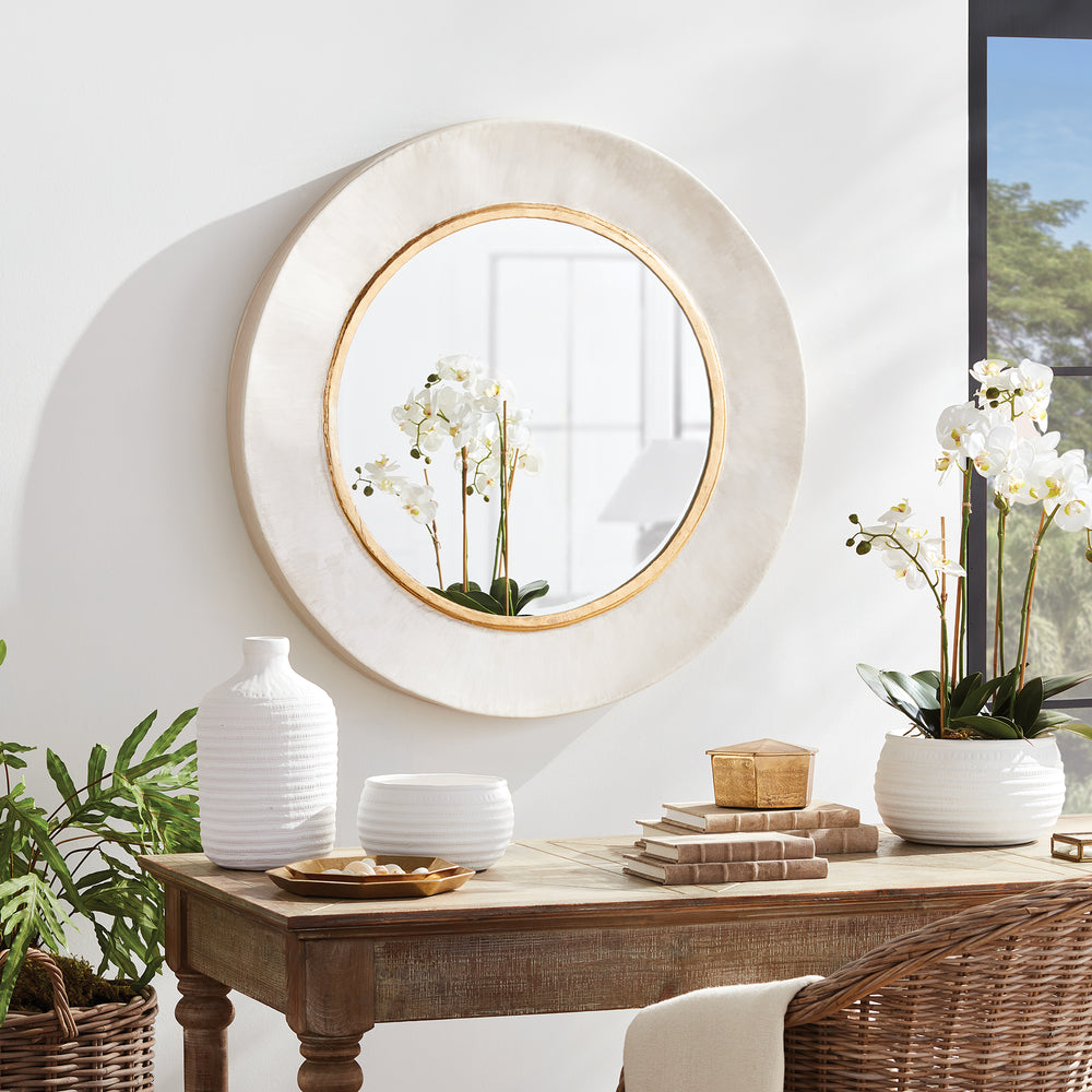 Oversized round white and gold wall mirror styled above wood console table in bright transitional living space.