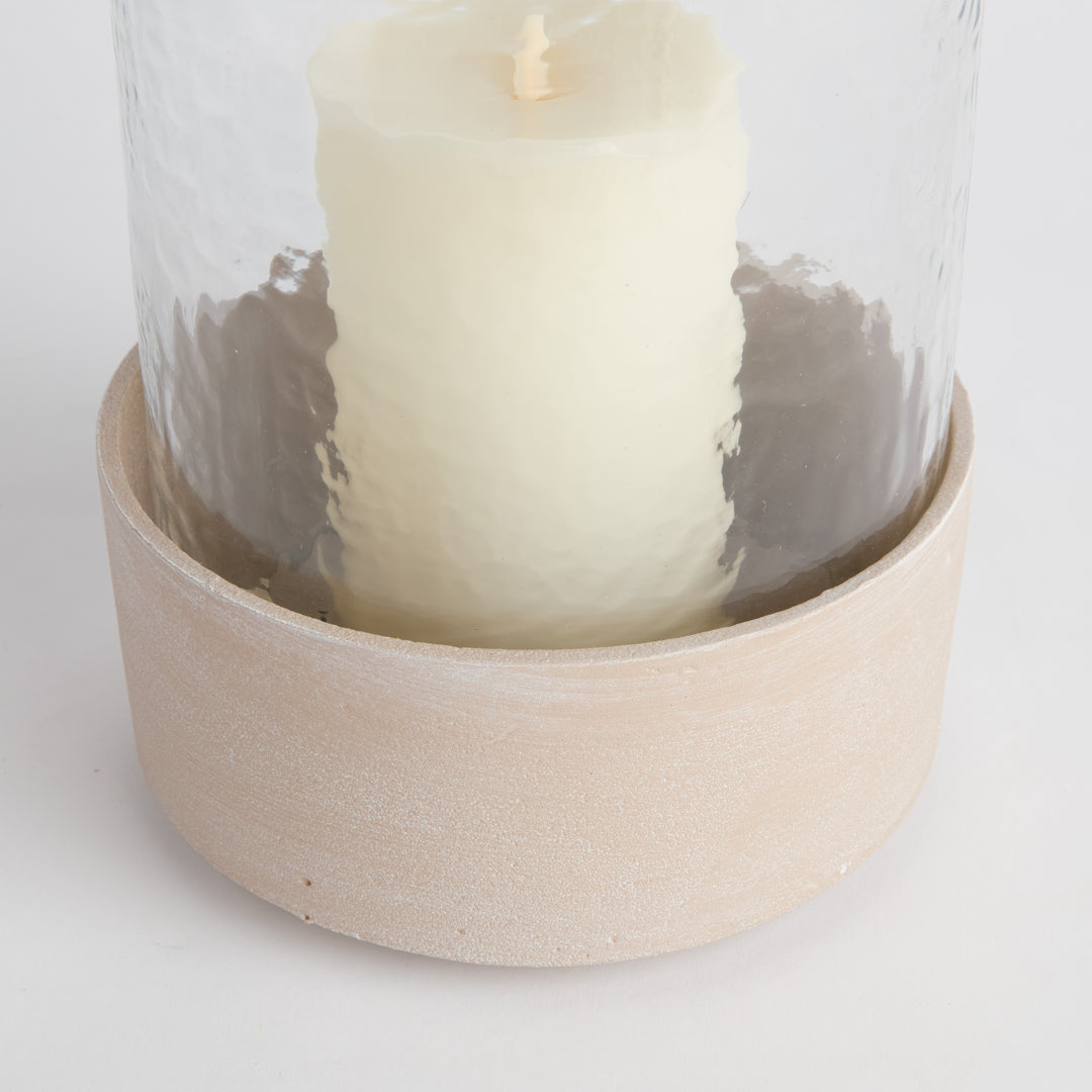 Close-up of pillar candle inside clear glass hurricane with textured sandstone-look aluminum base, Modern Organic style