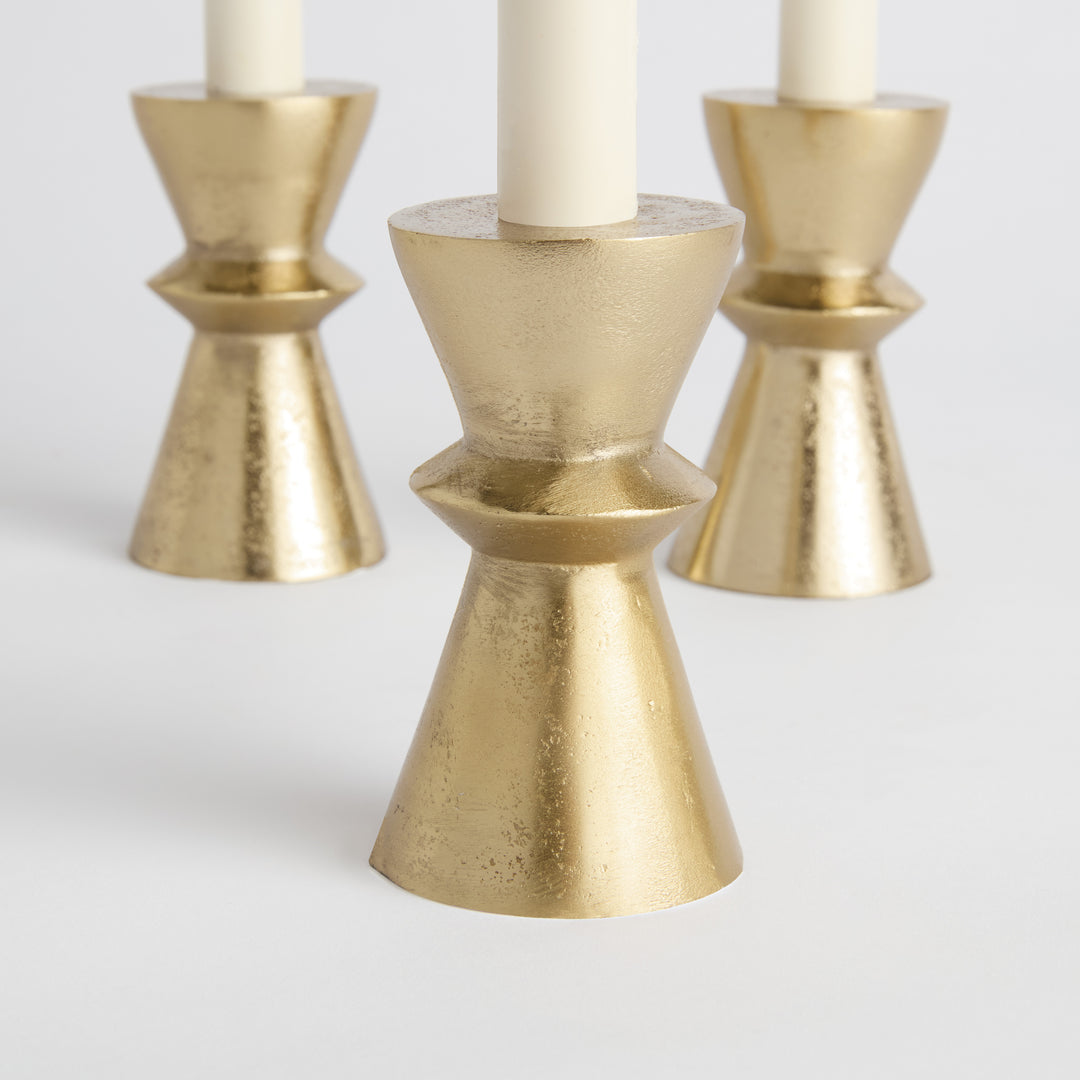Three gold aluminum taper holders shown from angled view with geometric silhouette and matte metallic finish – Minimalist