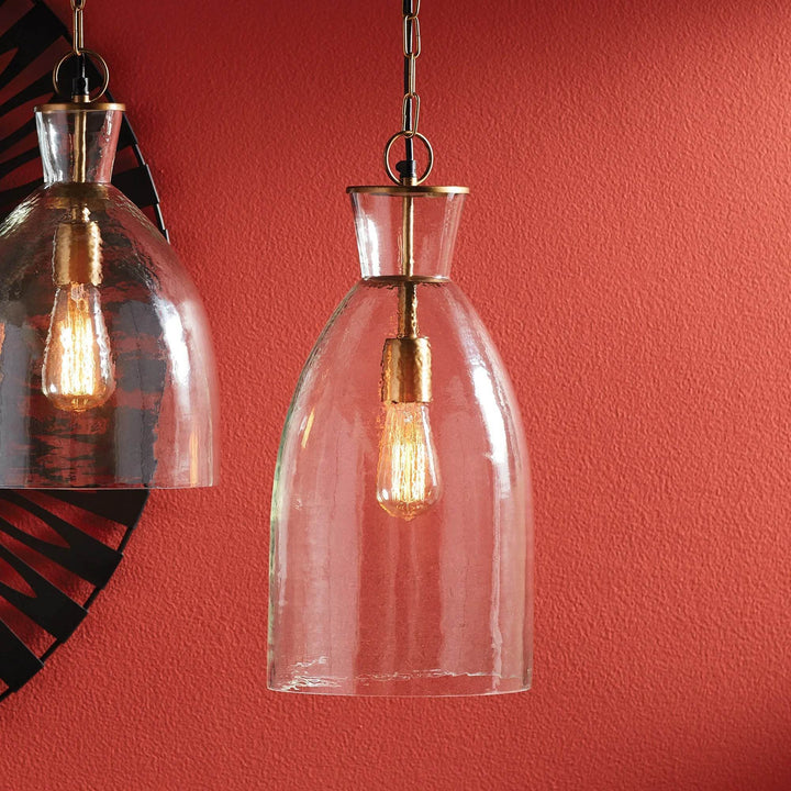 Tall seeded glass bottle pendant shown beside a bell pendant, with warm metal fittings against a red wall, Transitional style