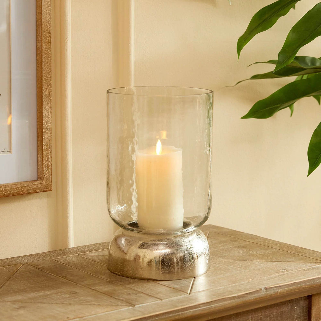 Glass hurricane candle holder with hammered finish and silver base, shown styled with pillar candle – Transitional Modern

