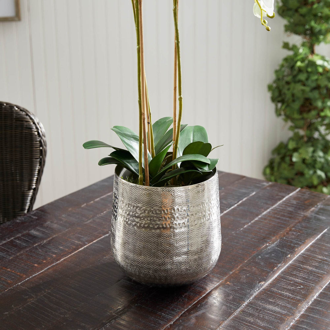 Textured cachepot styled with green foliage and stems, shown on dark wood surface – Modern Organic.

