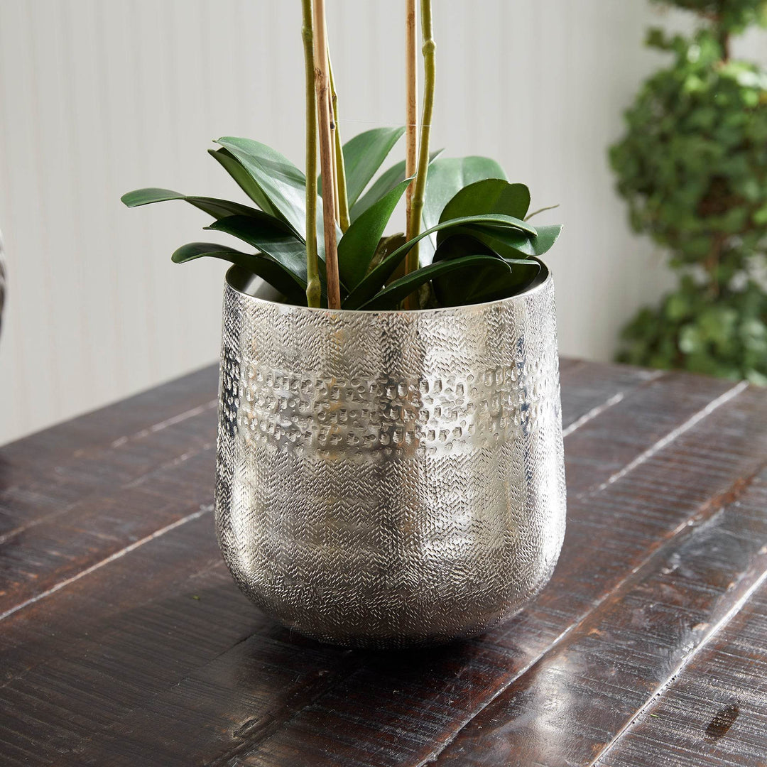 Side angle of silver metal cachepot with green plants styled on tabletop – Modern Organic.

