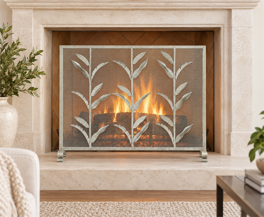 Silver botanical fireplace screen on fixed legs, shown before a glowing fireplace with a pale stone surround | Transitional