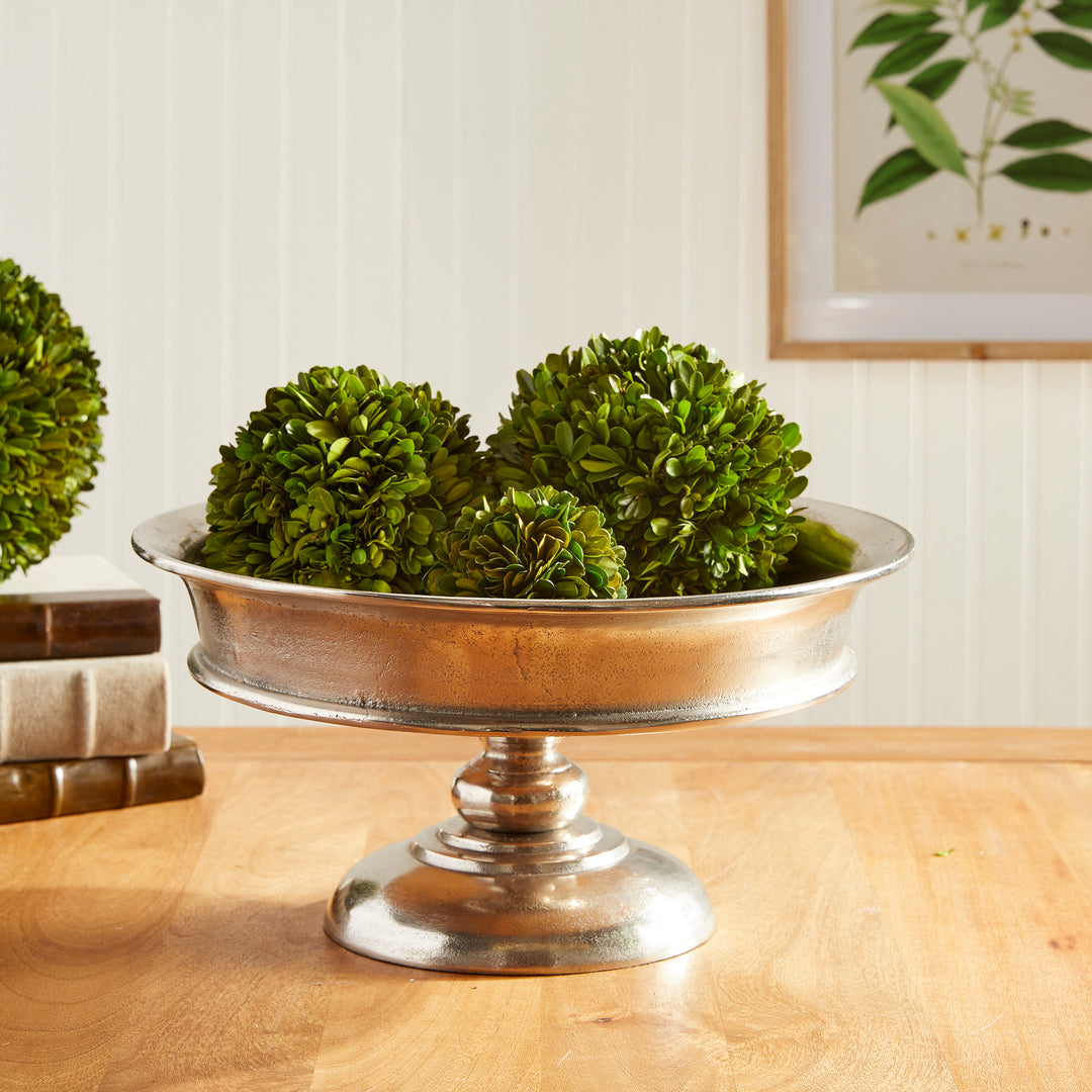 Decorative aluminum pedestal bowl filled with artificial green orbs on dining table – Modern Classic

