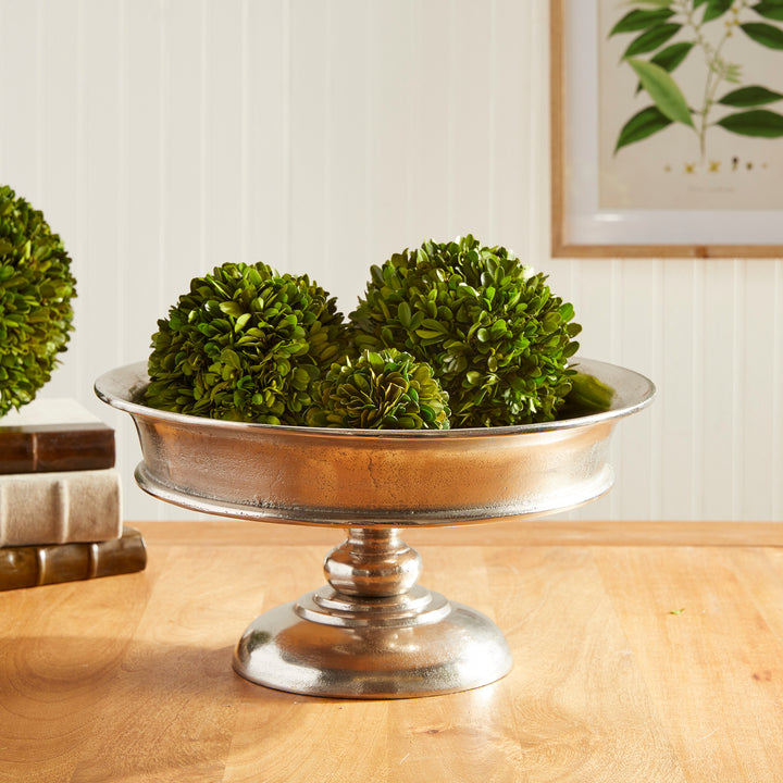Decorative aluminum pedestal bowl filled with artificial green orbs on dining table – Modern Classic

