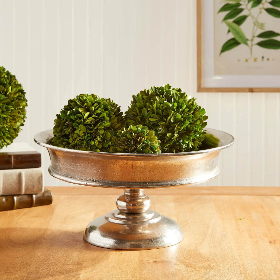 Decorative aluminum pedestal bowl filled with artificial green orbs on dining table – Modern Classic

