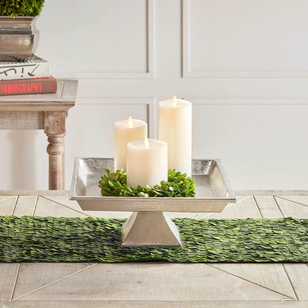 Silver pedestal tray styled with multiple white pillar candles, adding height and elegance to table decor.

