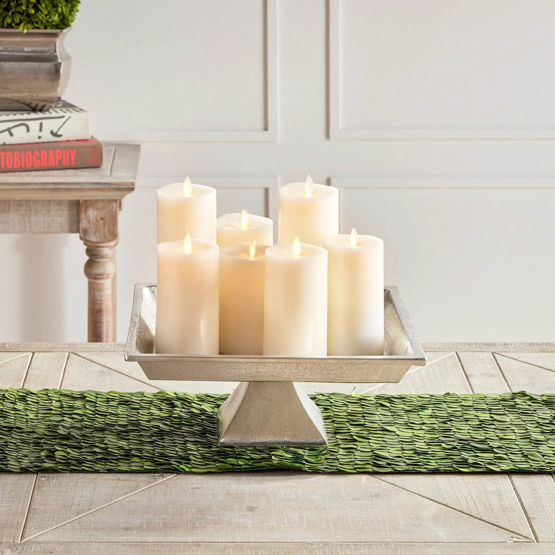Decorative silver pedestal tray with white pillar candles and greenery, styled for seasonal or everyday centerpiece decor.

