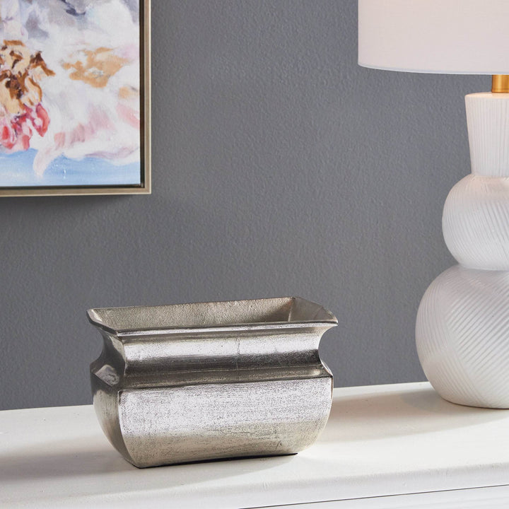 Rectangular antique silver vase displayed on console under artwork

