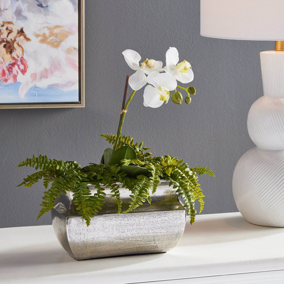 Sculptural silver vase styled with orchid and faux fern on console table

