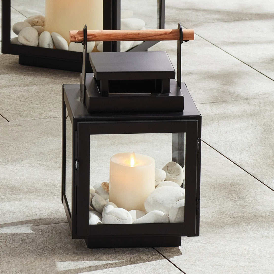 Small black outdoor lantern styled with candle and stones on patio