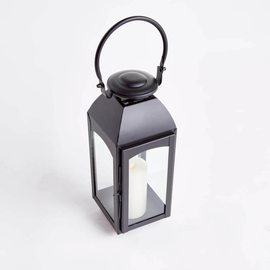 Small black outdoor lantern in iron, clear glass panels and ring handle, angled studio view with pillar candle – Transitional