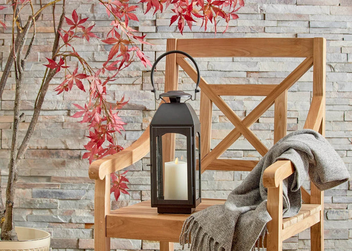 Front view of small black lantern with ring handle and pillar candle on bench; clear glass panes show steady glow in scene – Transitional Home