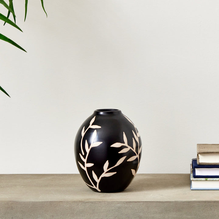 Small black terracotta vase with etched vine pattern on console surface beside stacked books – Modern Organic.
