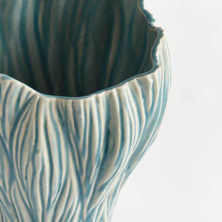Close view of blue reactive glaze over flowing ridges on a ceramic vase, showing its uneven upper edge, Coastal Transitional