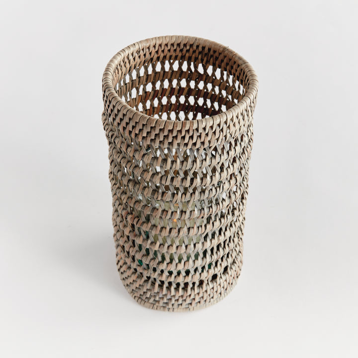 Angled view into a small graywash rattan hurricane, showing its open weave and round rim against plain white, Transitional
