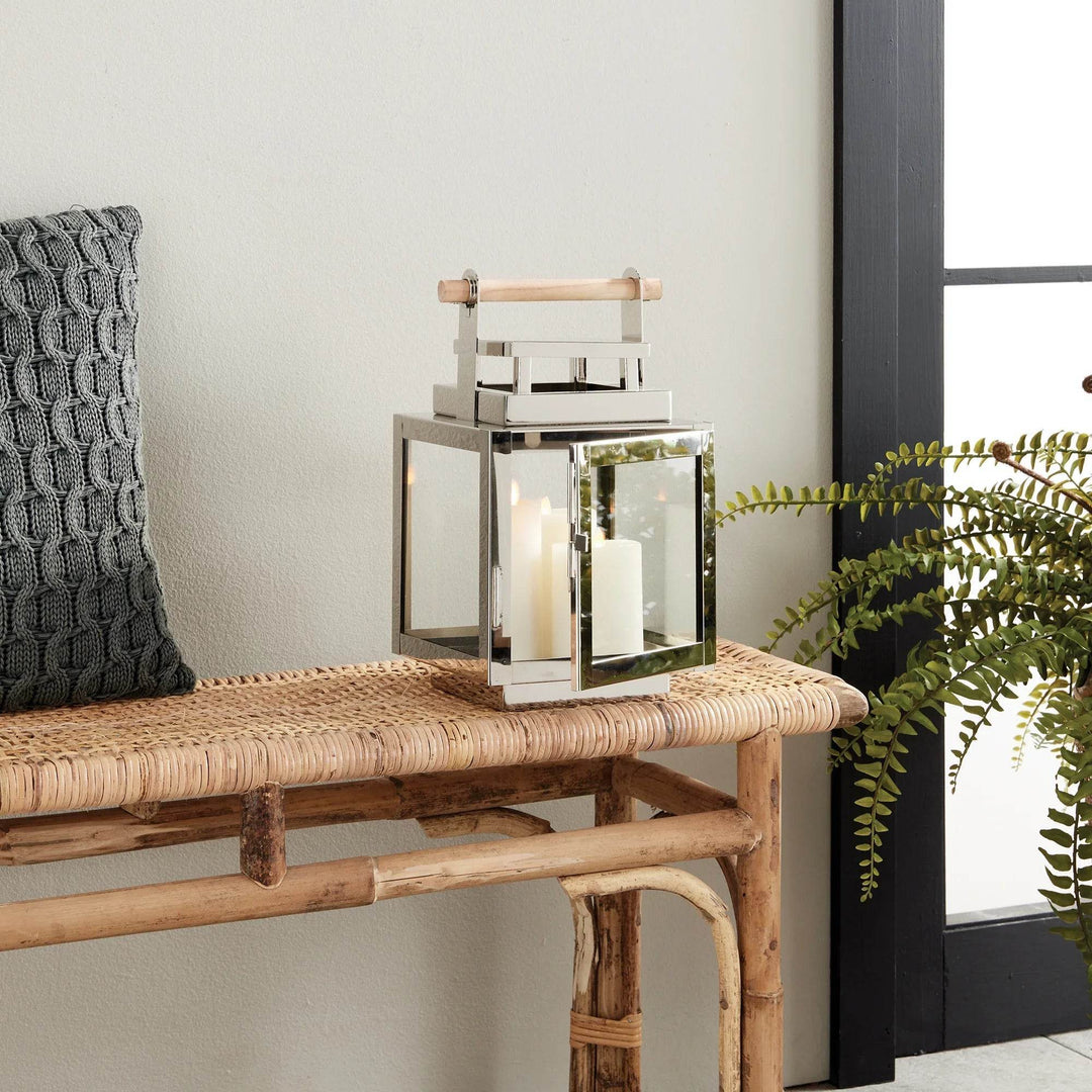 Silver outdoor lantern with teak handle displayed beside window and greenery