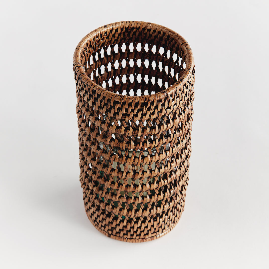 Angled view into a small warm brown rattan hurricane, showing its open weave and round rim against plain white, Transitional