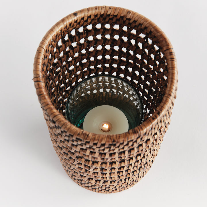 Top view into a small warm brown rattan hurricane showing a candle within its glass insert and open woven sides, Transitional