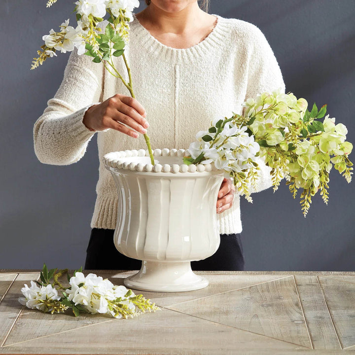 Small white ceramic flared vase shown with hands arranging floral stems inside, artisan handmade in Italy decor styling piece – French Country.

